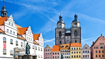 Staty av Luther mot medeltida bebyggelse och en klarblå himmel, i Wittenberg.